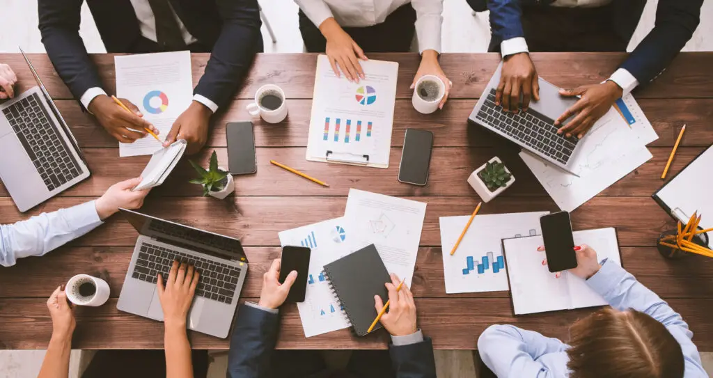 Team arbeitet an einem Tisch mit Laptops, Notizen und Diagrammen und bespricht Schritte im WordPress Projekt Ablauf