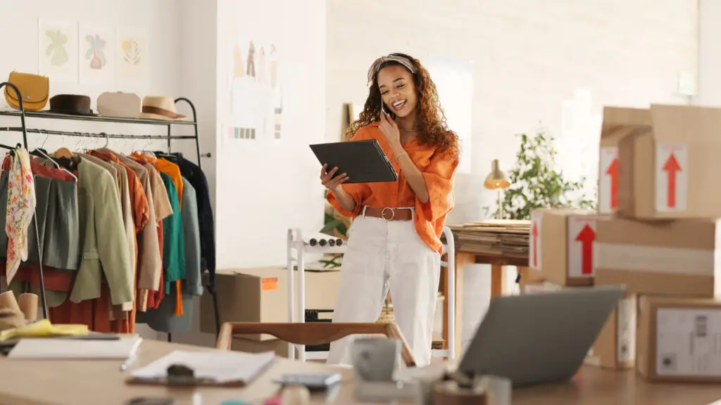 Modehändlerin in einem Online-Shop mit Tablet, Kleidung und Versandpaketen, passend zum Thema WooCommerce mit Elementor