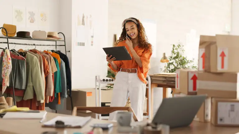 Modehändlerin in einem Online-Shop mit Tablet, Kleidung und Versandpaketen, passend zum Thema WooCommerce mit Elementor